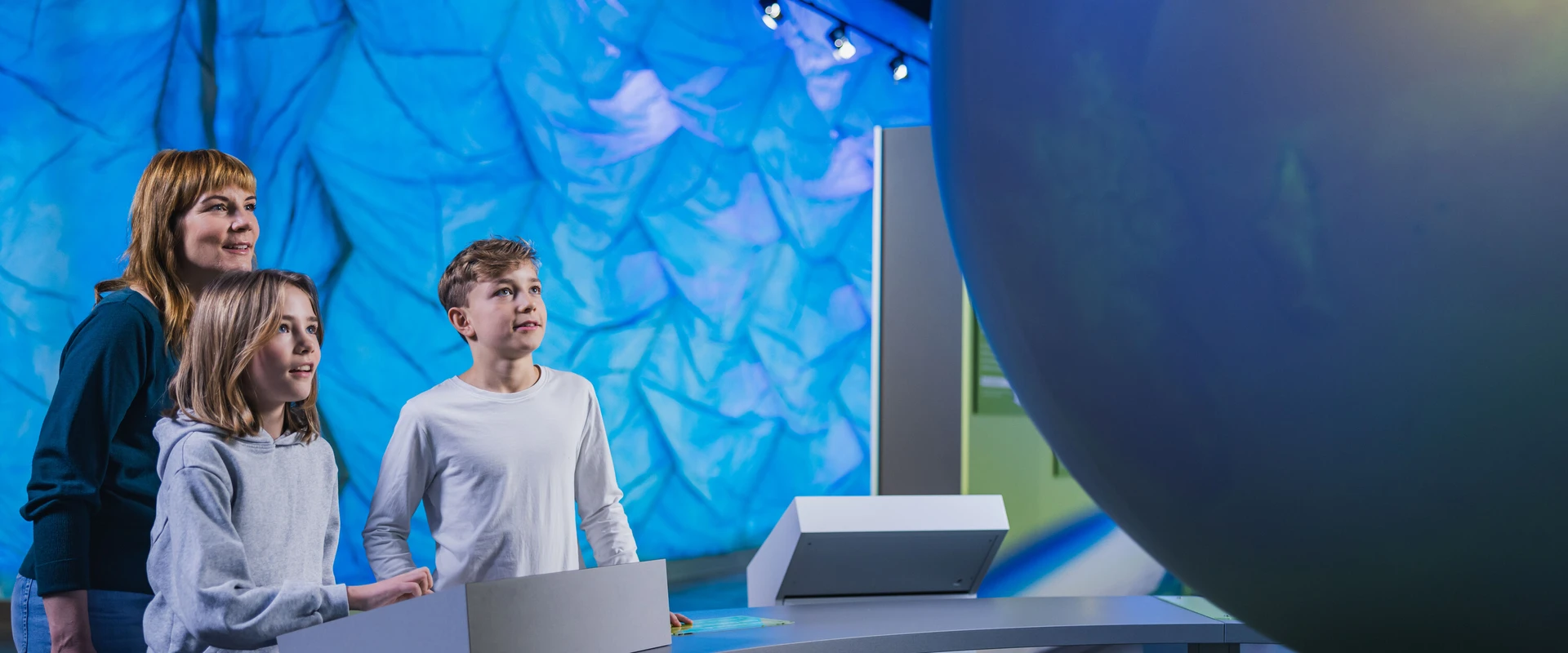 Mutter m&iacute;t zwei Kindern am Steuerungsmonitor des interaktiven Globus.